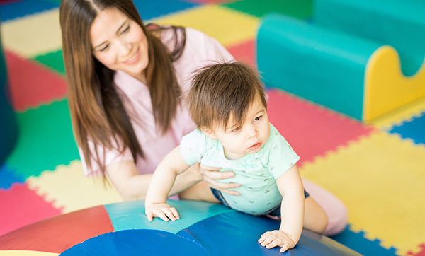 young child climbing on colorful play equipment while caregiver supports them in a playful learning environment promoting child development and motor skills for ages five and under