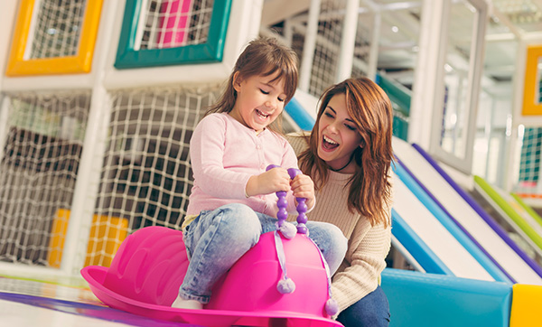 young girl enjoying playtime with mother on pink slide toy in colorful indoor playground 2 happy moments 2 smiles